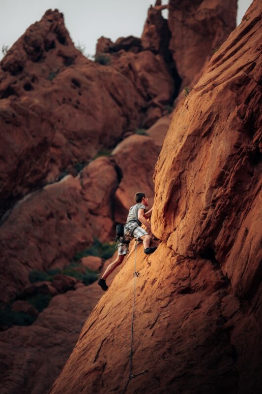 man in white shirt climbing brown rock mountain during daytime