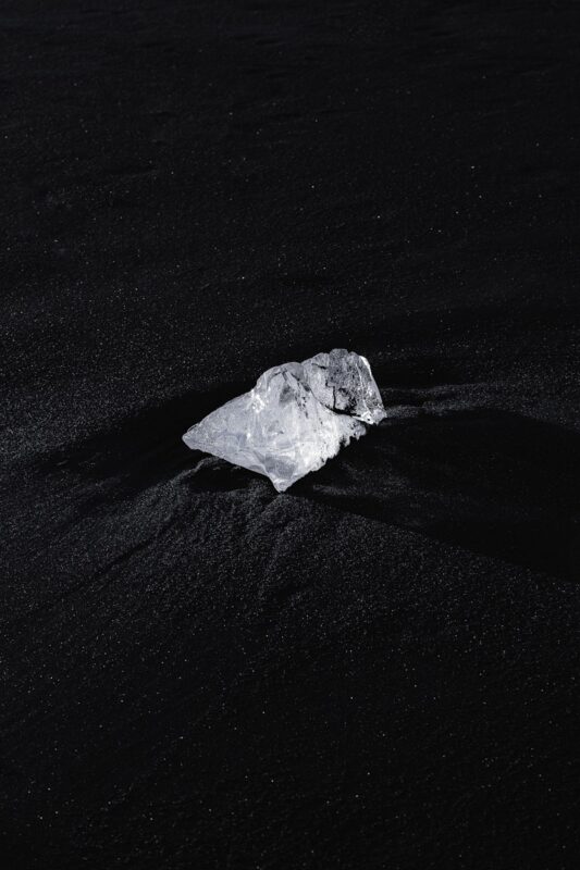Photo by Robert Arnar a piece of ice sitting on top of a black sand beach