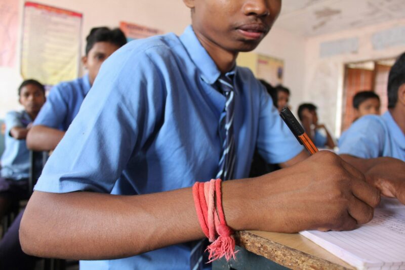 a man in a blue shirt and tie writing on a piece of paper