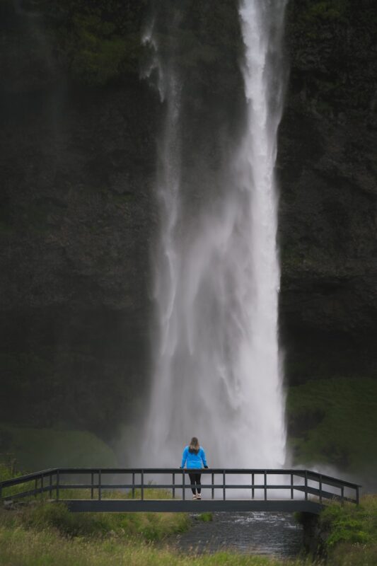 A person standing on a bridge looking at a waterfall